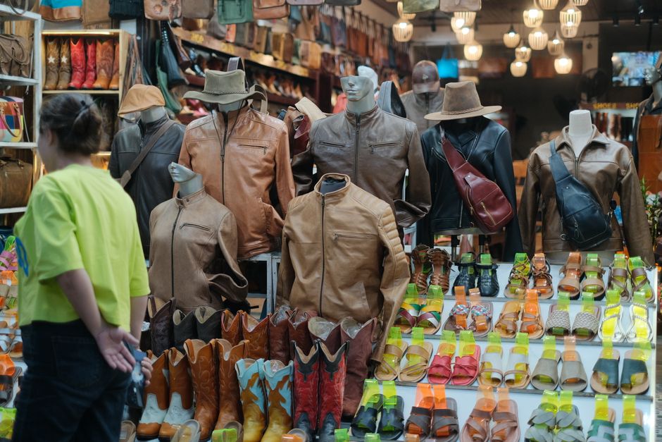 Imagem de uma loja de calçados e roupas com manequins exibindo jaquetas e chapéus, além de uma variedade de sapatos coloridos na vitrine, capturando o tema de moda e comércio varejista.