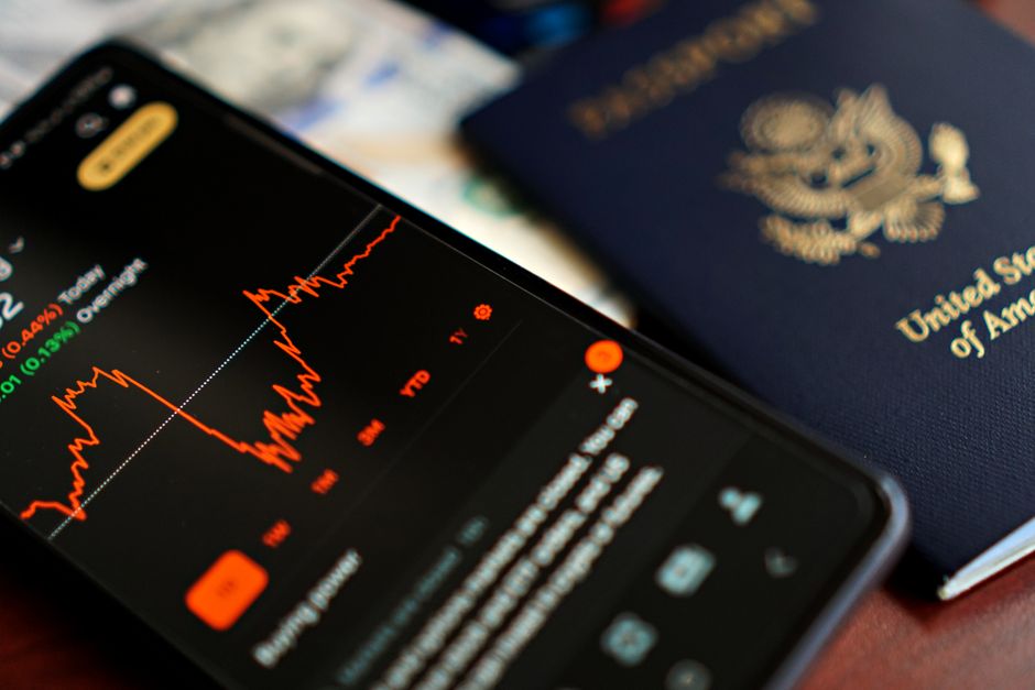 Imagem de um celular exibindo gráficos de mercado financeiro ao lado de um passaporte dos Estados Unidos, ilustrando temas de investimentos internacionais e planejamento financeiro.