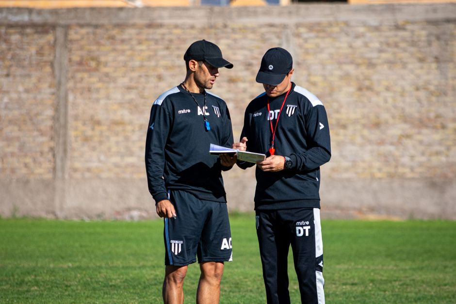 Dois treinadores de futebol discutindo estratégias durante treino ao ar livre, enfatizando planejamento e preparação esportiva.
