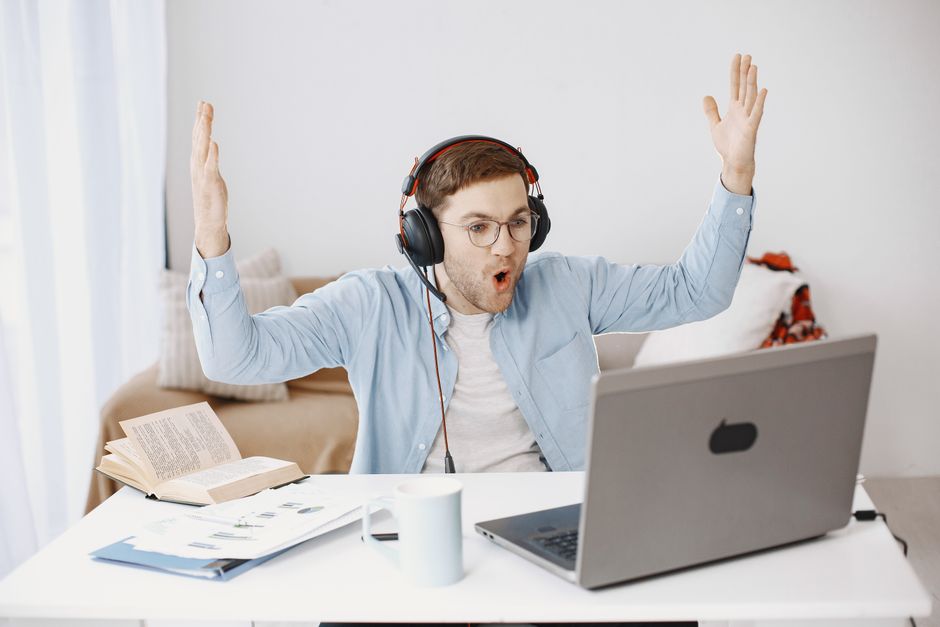 Homem assistindo a um webinar ou aula online com celebração de sucesso, em ambiente caseiro.