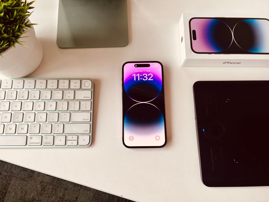 Imagem de uma estação de trabalho moderna com smartphone, teclado, tablet e caixa de um iPhone, ideal para ilustrar produtividade e tecnologia no ambiente profissional.