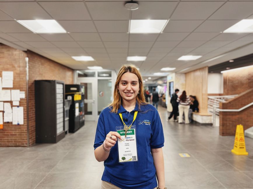 Jovem estudante orgulhosa exibindo seu credencial acadêmico em ambiente de evento educacional ou olimpíada de conhecimento.