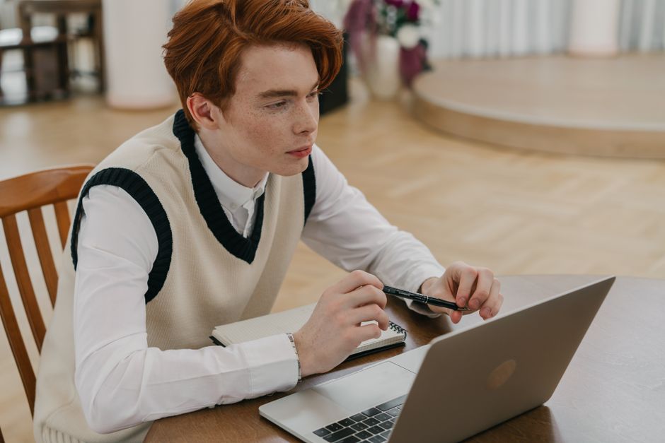 Jovem estudando ou trabalhando com foco em planejamento ou estudos online, em ambiente com iluminação natural e decoração sutil ao fundo.