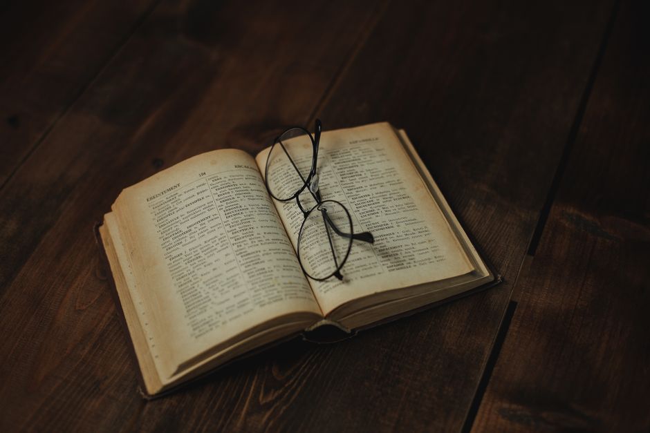 Livro aberto com óculos sobre uma superfície de madeira, simbolizando leitura, estudo ou pesquisa.