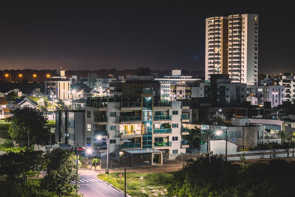 Visão noturna de um bairro residencial com edifícios e iluminação urbana, destacando o cenário urbano à noite.