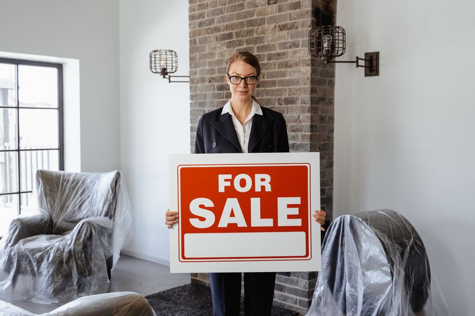 Mulher de negócios segurando placa de venda em ambiente interno elegante, simbolizando fechamento de negociação imobiliária.
