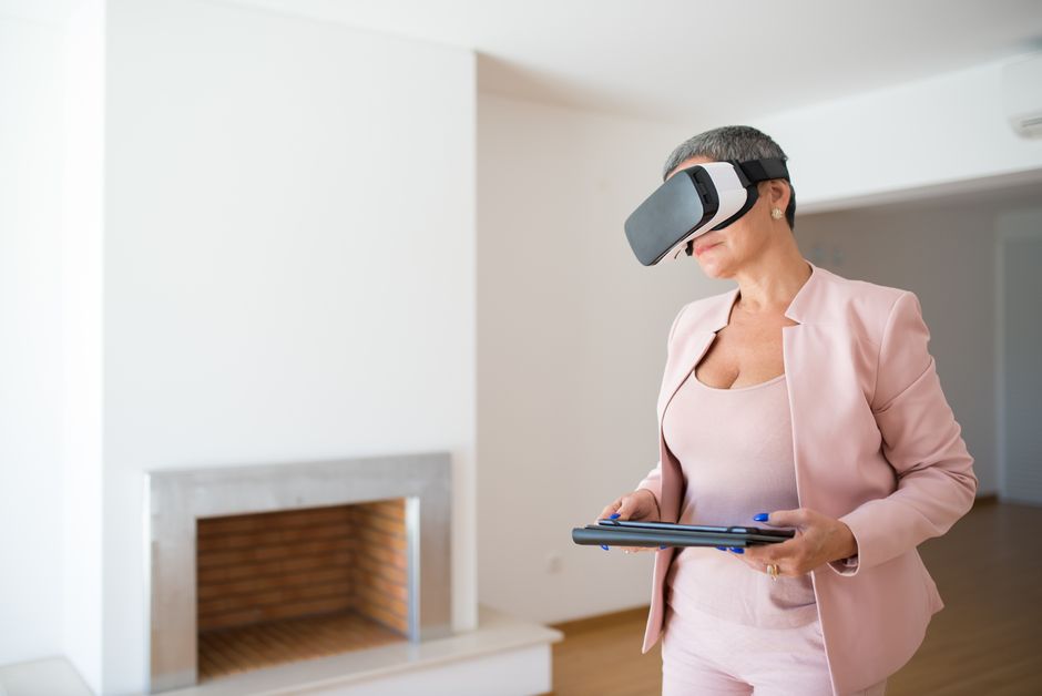 Mulher usando óculos de realidade virtual ao mesmo tempo em que utiliza um tablet em um ambiente moderno e minimalista.