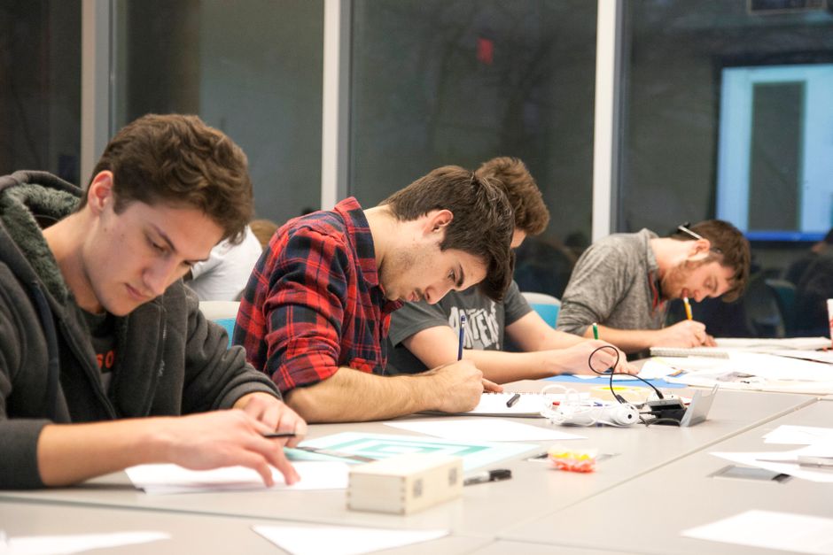 Grupo de jovens concentrados em projeto de tecnologia ou engenharia em ambiente de sala de aula ou laboratório.