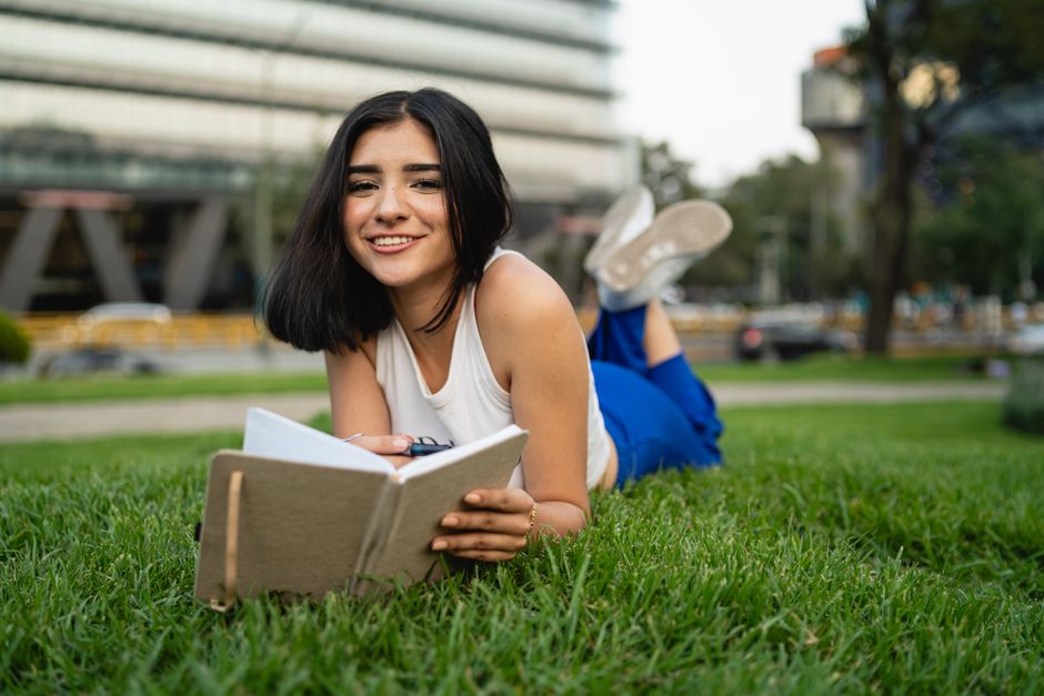 Jovem mulher lendo um livro ao ar livre, apreciando um momento de relaxamento na natureza.