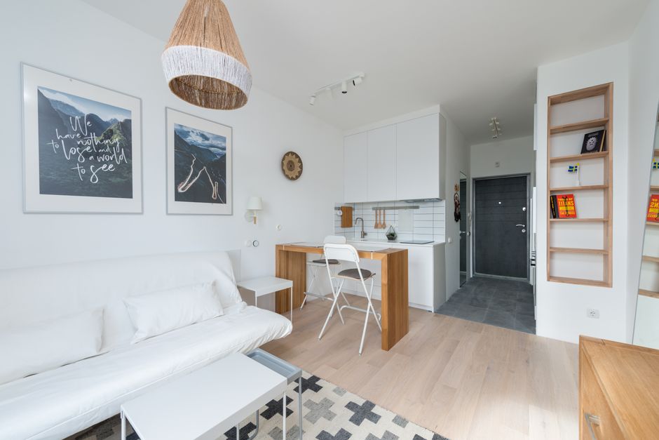 Imagem de um espaço de convivência moderno e minimalista dentro de um apartamento, com área de estar e cozinha integradas.