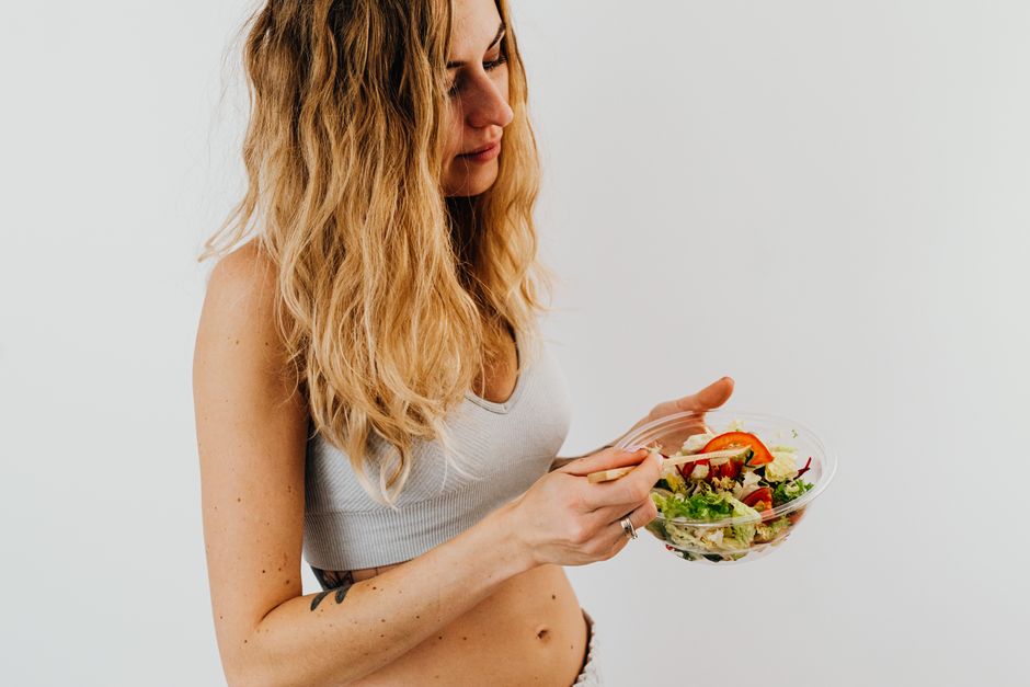 Mulher com cabelo loiro longo desfrutando de uma salada fresca e leve, retratando bem-estar e alimentação saudável.