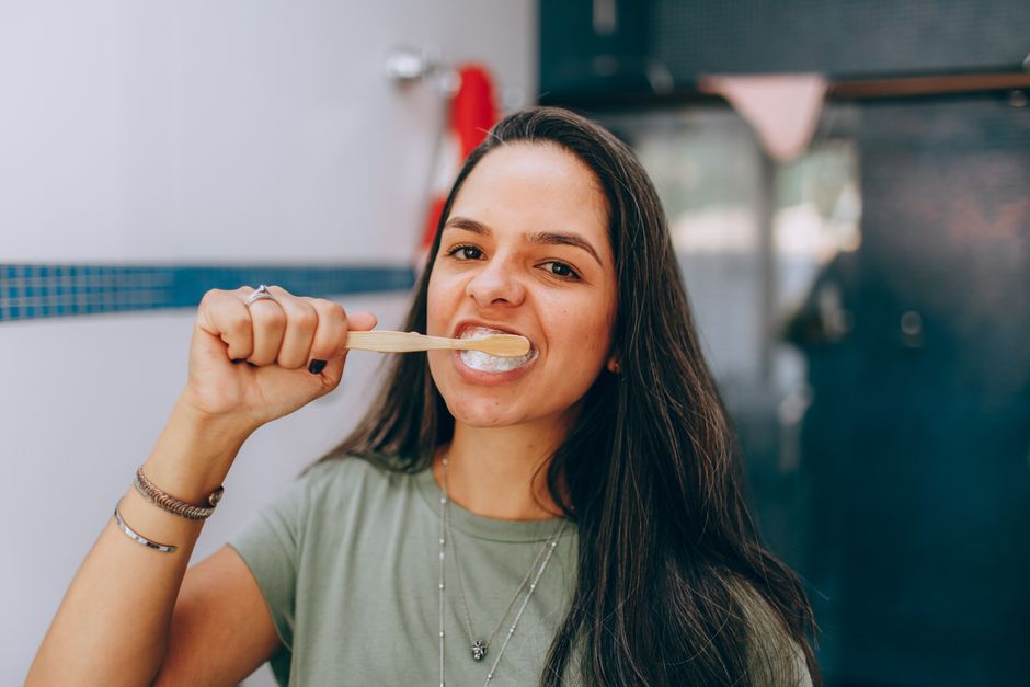 Jovem sorridente escovando os dentes com uma escova de bambu, promovendo saúde bucal natural.
