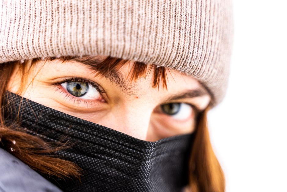 Close-up de uma pessoa usando máscara e gorro, transmitindo uma sensação de cuidado e proteção durante a pandemia.