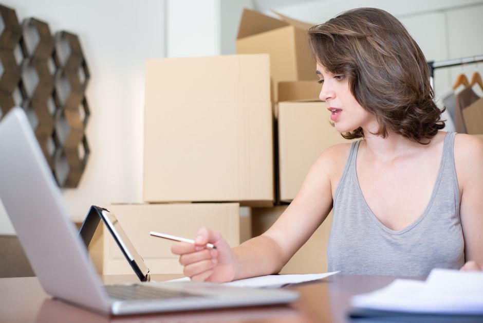 Mulher trabalhando de forma organizada e focada em um ambiente de escritório com caixas de mudança ao fundo, simbolizando transição ou organização de negócios.