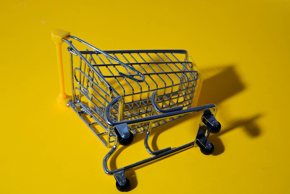 Carrinho de supermercado vazio sobre fundo amarelo, simbolizando consumo ou compras.