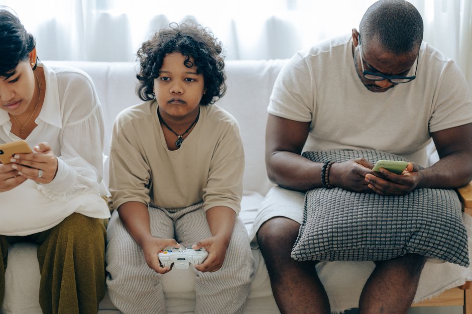 Família usando dispositivos eletrônicos no sofá em uma situação de lazer e tecnologia em casa.