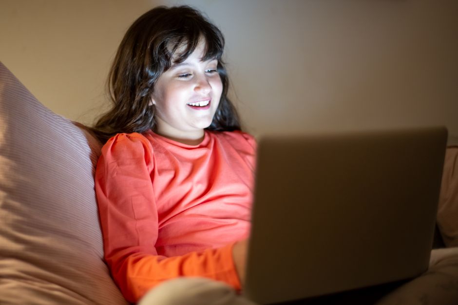Menina sorridente assistindo a conteúdo em um laptop, transmitindo uma sensação de diversão e engajamento digital.