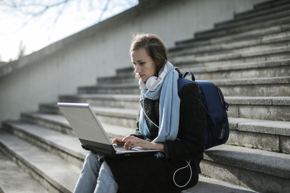Mulher jovem usando laptop ao ar livre em ambiente urbano, simbolizando estudo ou trabalho remoto.