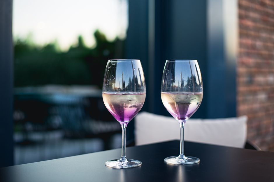 Duas taças de vinho com gelo e uma tonalidade roxa, em um ambiente interno com iluminação natural, sugerindo um momento de relaxamento ou celebração.