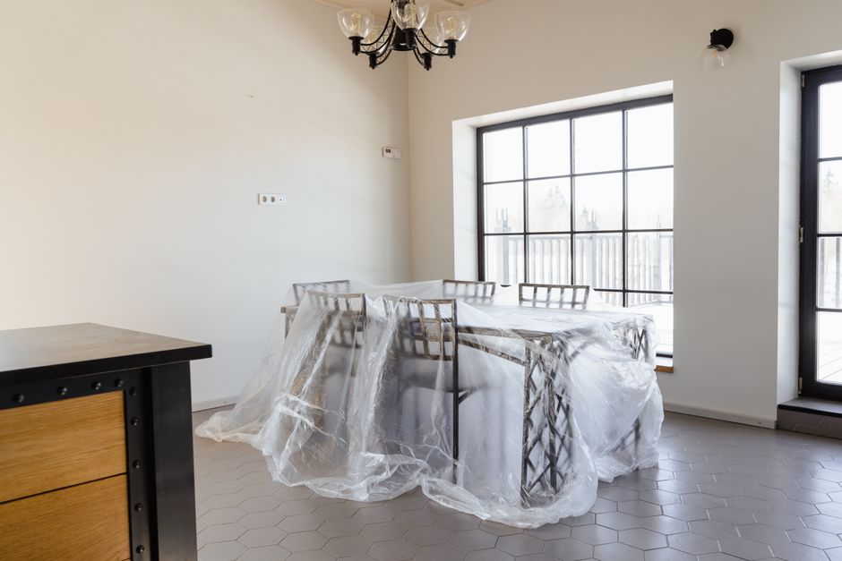 Sala de jantar vazia com mesa protegida por plástico, pronta para uma reforma ou limpeza profunda, com iluminação natural e decoração minimalista.