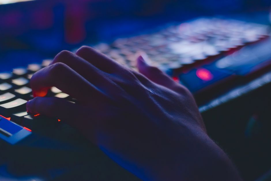 Pessoa utilizando um teclado iluminado em um ambiente com luzes de baixa intensidade, simbolizando tecnologia e inovação digital.