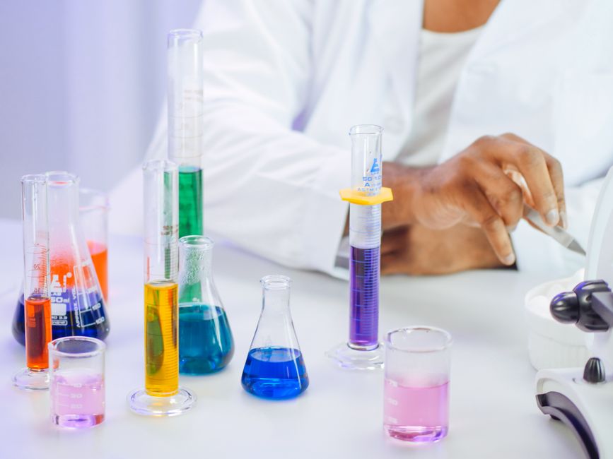 Imagem de um laboratório de ciências com tubos de ensaio coloridos e um profissional realizando observações, representando pesquisa e inovação científica.