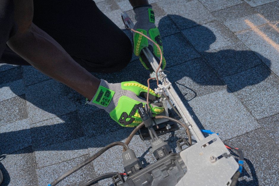 Homem ajustando ou instalando um equipamento elétrico ou sistema de energia em uma área externa, possivelmente relacionada a energia solar ou manutenção técnica.