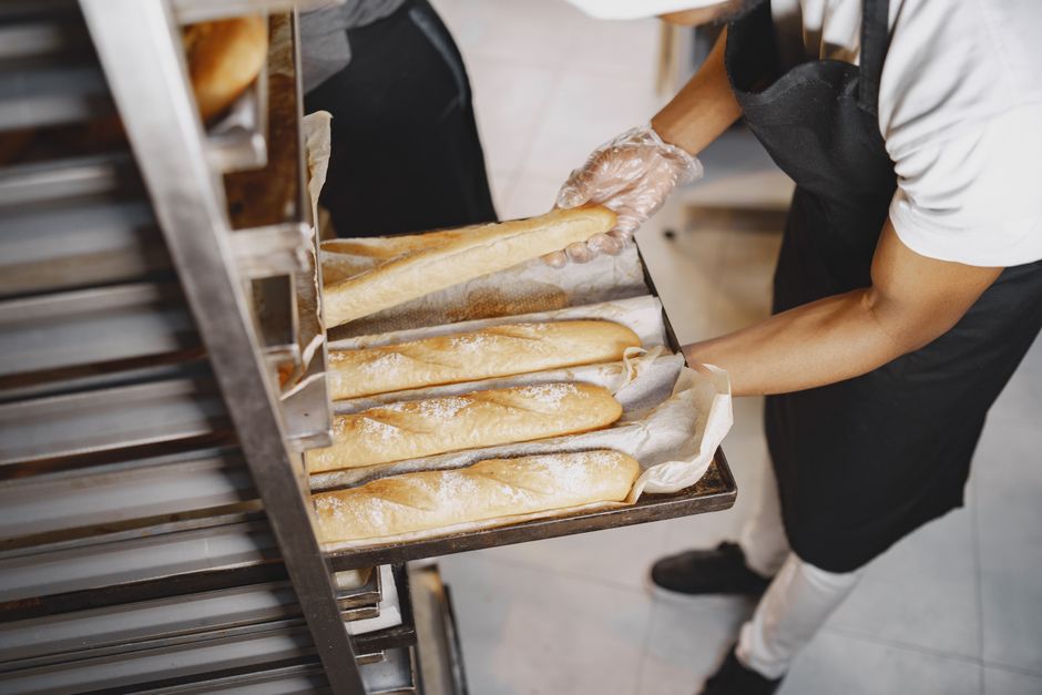 Pessoa preparando e levando pães recém-assados em uma padaria artesanal.