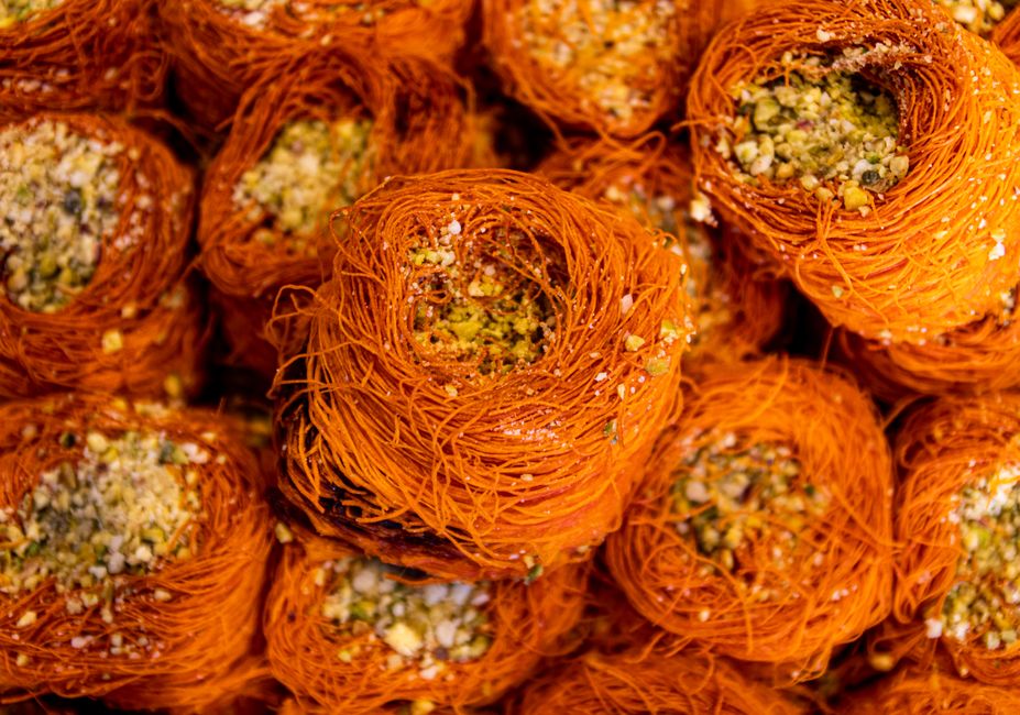 Doces tradicionais turcos de “Künefe” com camada de queijo e cobertura crocante de pistache, servidos em uma mesa festiva.