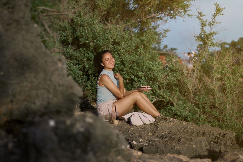 Mulher sorrindo sentada em um ambiente natural, aproveitando um momento de descanso ao ar livre.