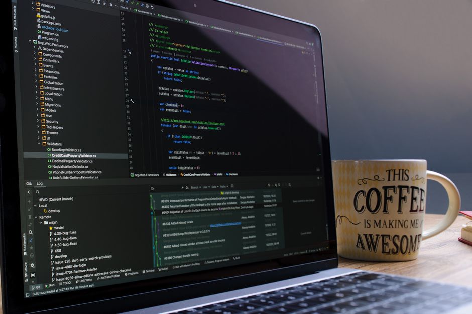 Imagem de um ambiente de trabalho com um laptop exibindo código de programação, acompanhado de uma caneca com mensagem motivacional, representando tecnologia e desenvolvimento de software.