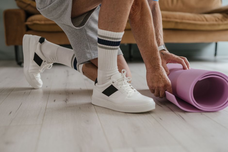 Pessoa ajustando o tapete de yoga em um ambiente doméstico, representando cuidados com saúde e bem-estar em casa.