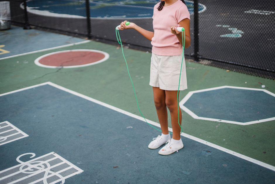 Criança brincando com corda de pular em uma quadra de esportes ao ar livre, destacando momentos de lazer infantil.