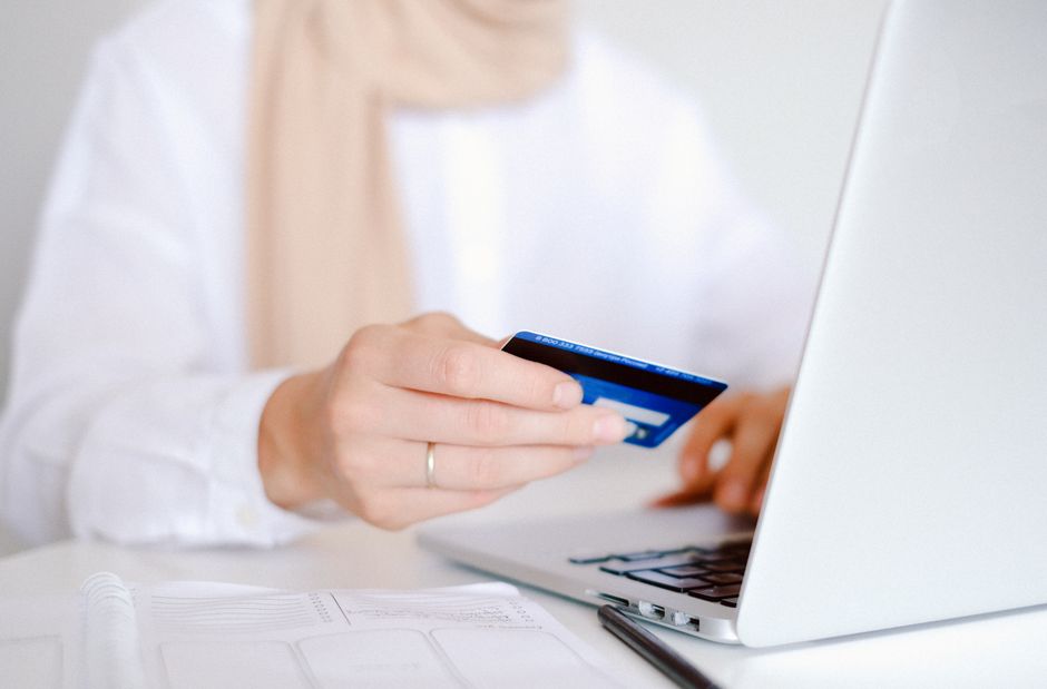 Pessoa realizando uma compra online usando o computador e o cartão de crédito, representando comércio eletrônico e transações digitais.