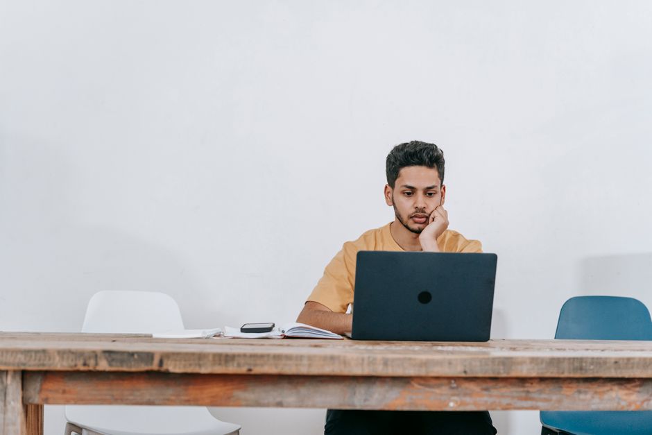 Jovem concentrado trabalhando em um laptop em um ambiente de escritório minimalista, ideal para artigos sobre produtividade, trabalho remoto ou educação online.