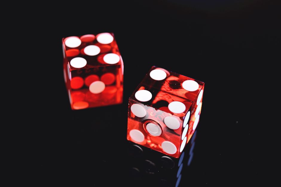 Imagem de dois dados vermelhos com pontos brancos sobre um fundo escuro, simbolizando azar ou jogo de azar.