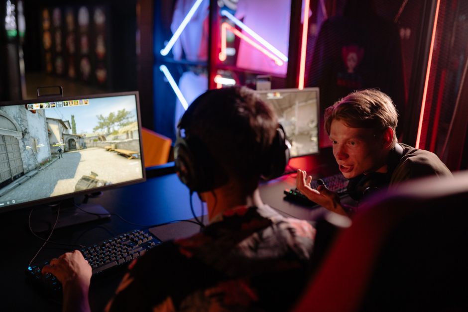 Dois jovens jogadores de eSports conversando durante uma partida de videogame em um ambiente com iluminação de neon.