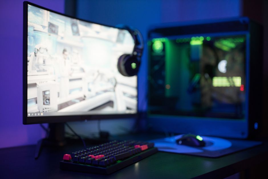 Configuração de uma estação de trabalho para jogos ou edição com dois monitores, teclado mecânico e headset, em um ambiente com iluminação colorida.