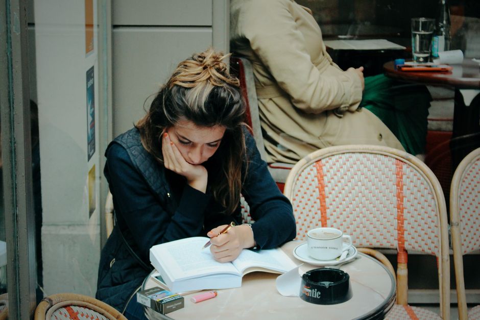 Mulher estudando ou lendo em um café, demonstrando concentração e reflexão em um ambiente de lazer ou estudo.