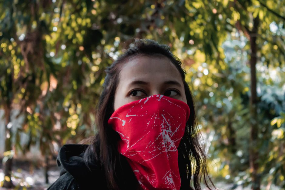 Mulher usando máscara facial vermelha em ambiente ao ar livre, simbolizando cuidados com saúde e proteção individual.