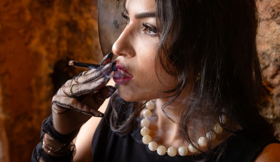 Mulher elegante usando luvas de renda, joias e cigarro, transmitindo uma atmosfera de sofisticação e mistério.