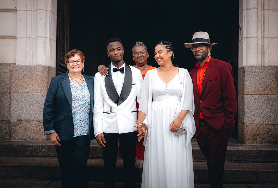 Grupo de pessoas sorrindo em celebração na entrada de um edifício com aspecto clássico, representando momentos de comemoração e união familiar ou social.