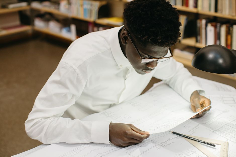 Homem estudando ou analisando projetos técnicos em ambiente de bibliotecas ou escritórios acadêmicos.