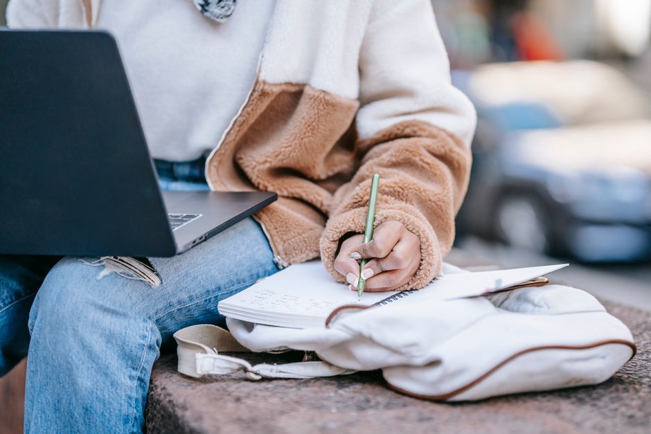 Pessoa estudando ou fazendo anotações ao ar livre, com laptop ao lado, sugerindo foco em aprendizado ou trabalho remoto.