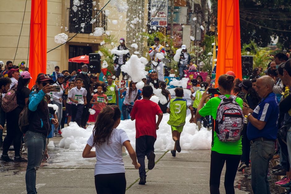 Crianças e adultos participando de uma atividade divertida com espuma em uma rua urbana, destacando um evento comunitário ao ar livre