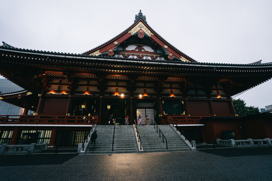 Imagem de um templo tradicional japonês com arquitetura elegante, escadaria central e pessoas entrando na estrutura, evocando cultura e espiritualidade.