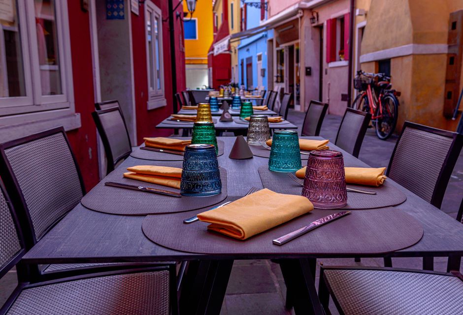 Capa de mesa ao ar livre em um restaurante com taças coloridas e talheres dispostos para um evento social ou refeição ao ar livre em uma rua vibrante.