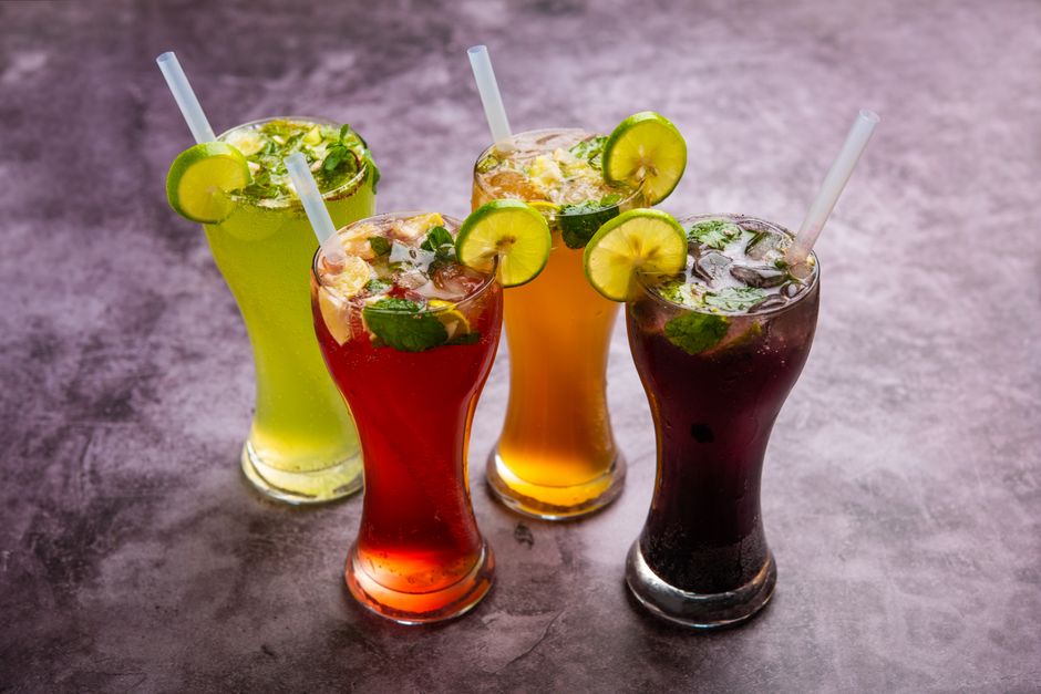 Imagem de quatro coquetéis coloridos decorados com rodelas de limão e hortelã, indicando uma atmosfera de festa ou celebração.