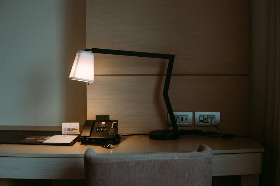 Imagem de uma mesa de trabalho com uma luminária moderna, telefone fixo e tomadas, ideal para ilustrar ambientes de trabalho ou escritórios corporativos.