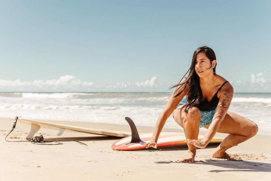 Mulher ajustando uma prancha de surf na areia de uma praia ensolarada, pronto para surfar.